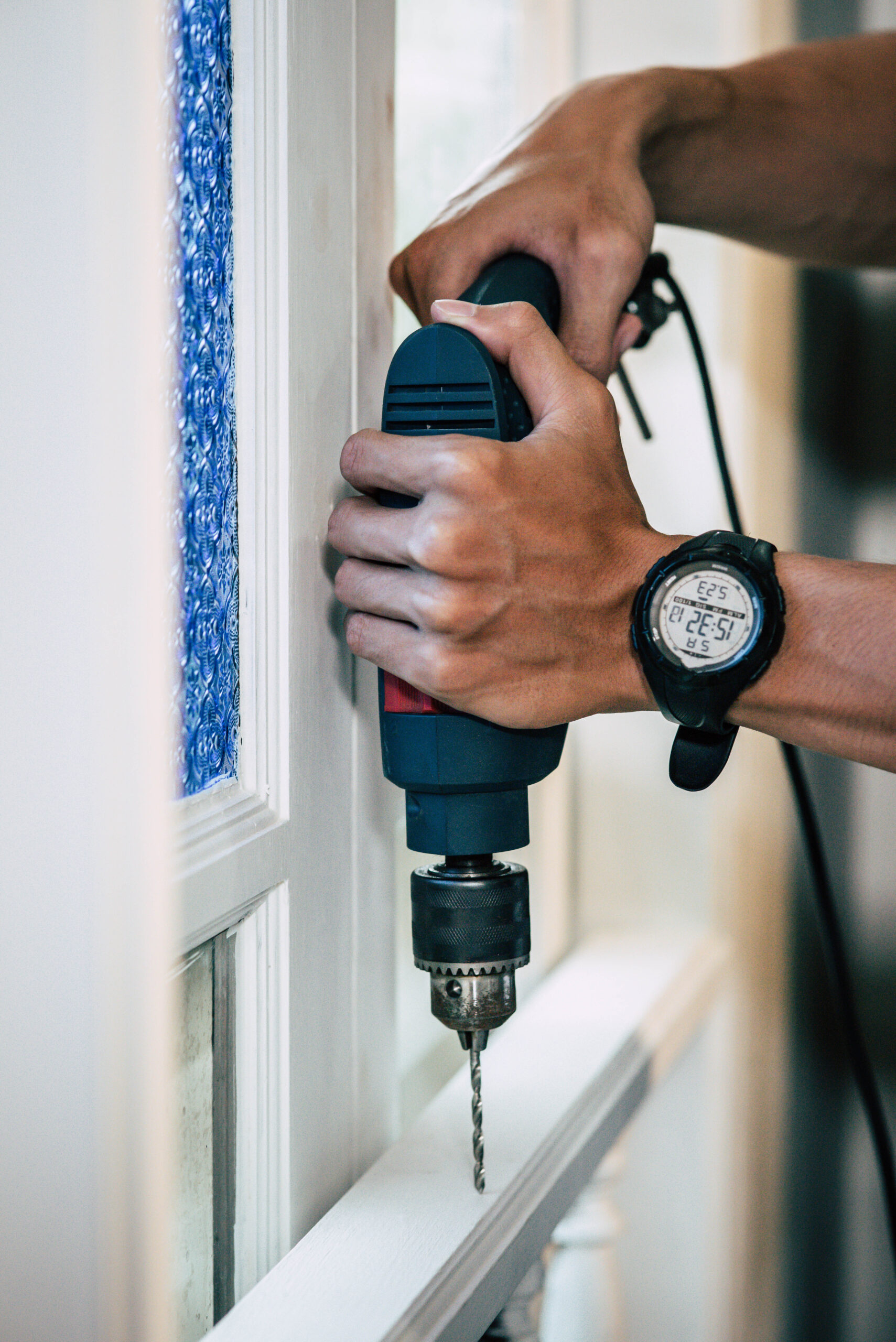 The carpenter holds the drill and drills the window. Selective focus.